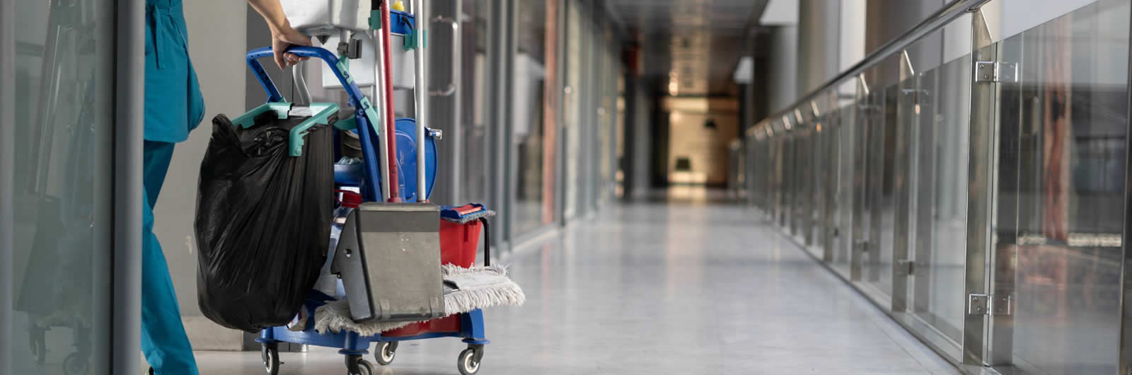 Limpieza corporativa: un operario con elementos de limpieza en pasillo de edificio moderno