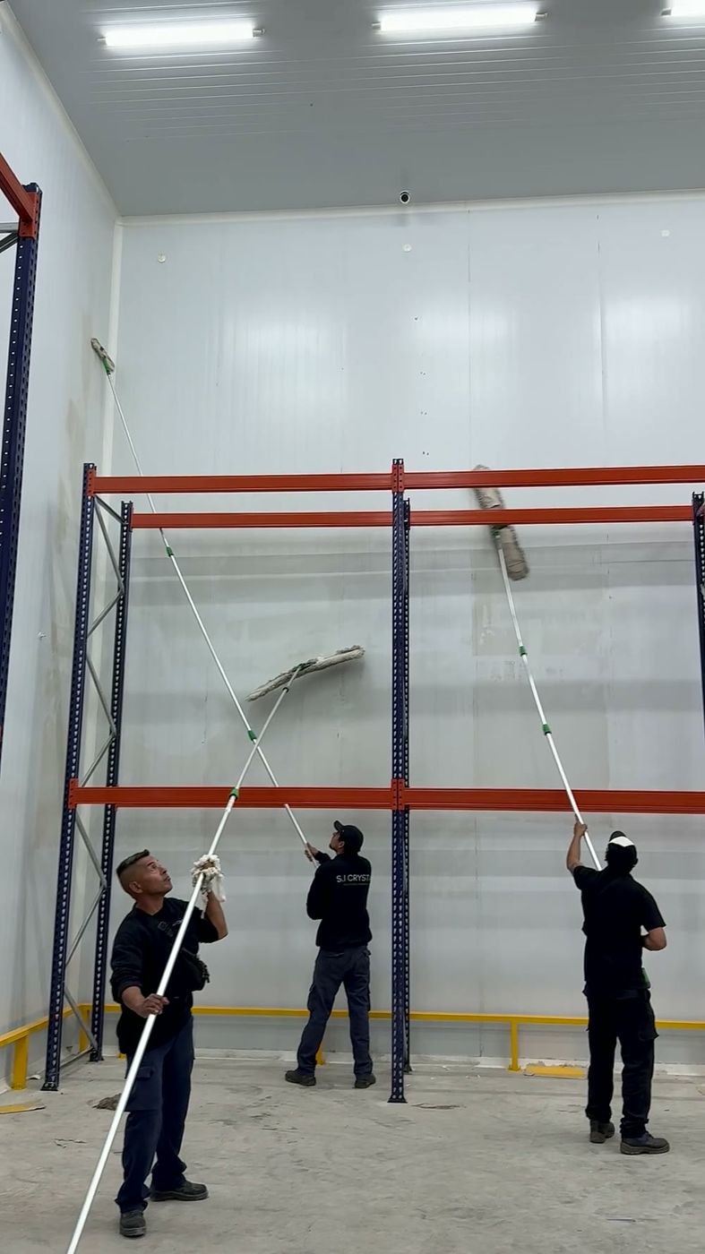 Equipo de Crystal limpiando paredes altas de un depósito con pértigas
